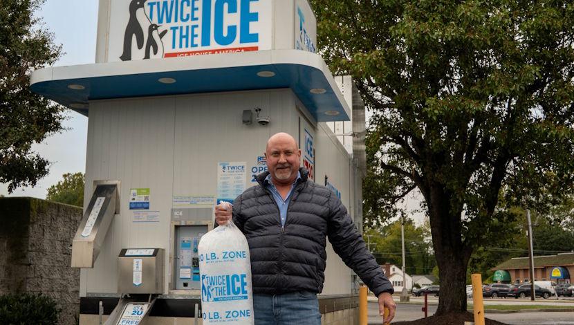 man holding "twice the ice" bag of ice in front of ice machine