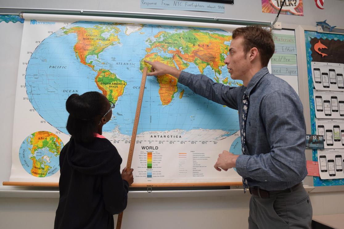 male student showing young girl a map as she points with a yard stick