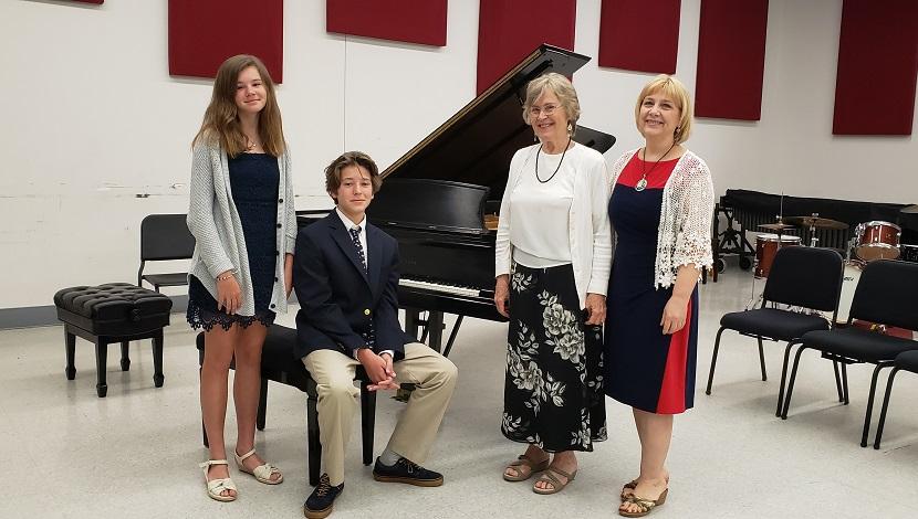 Two students next to piano and instructor