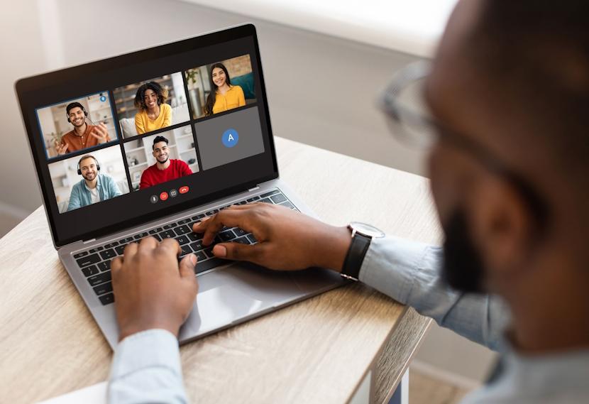  Person typing at computer while screen shows a virtual group meeting