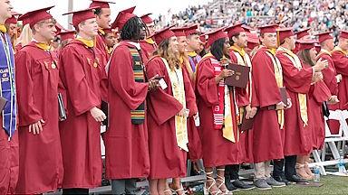students in regalia standing in Sea Gull Stadium during commencement cermony