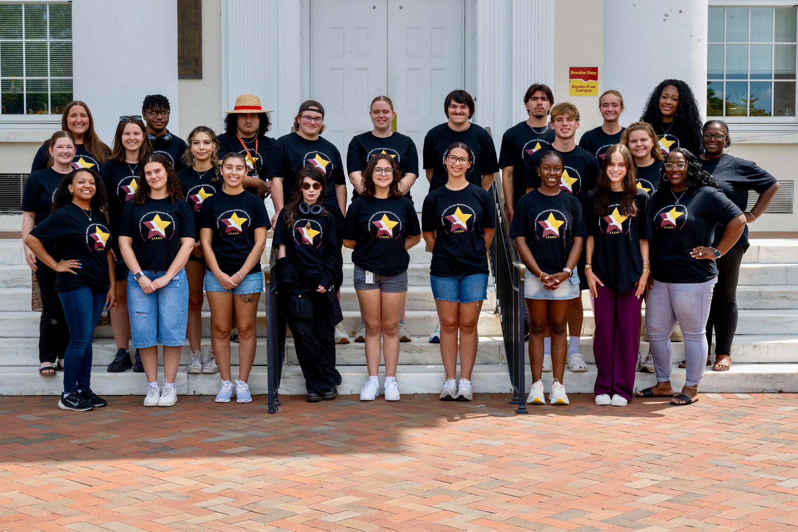 Salisbury University S.T.A.R.S. program members and staff pose together on campus steps, smiling and wearing matching black S.T.A.R.S. shirts.