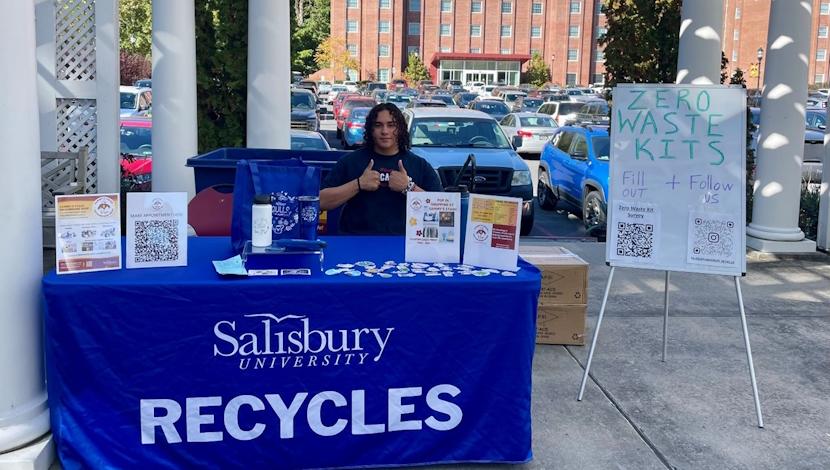 Student working a recycling event table giving thumbs up