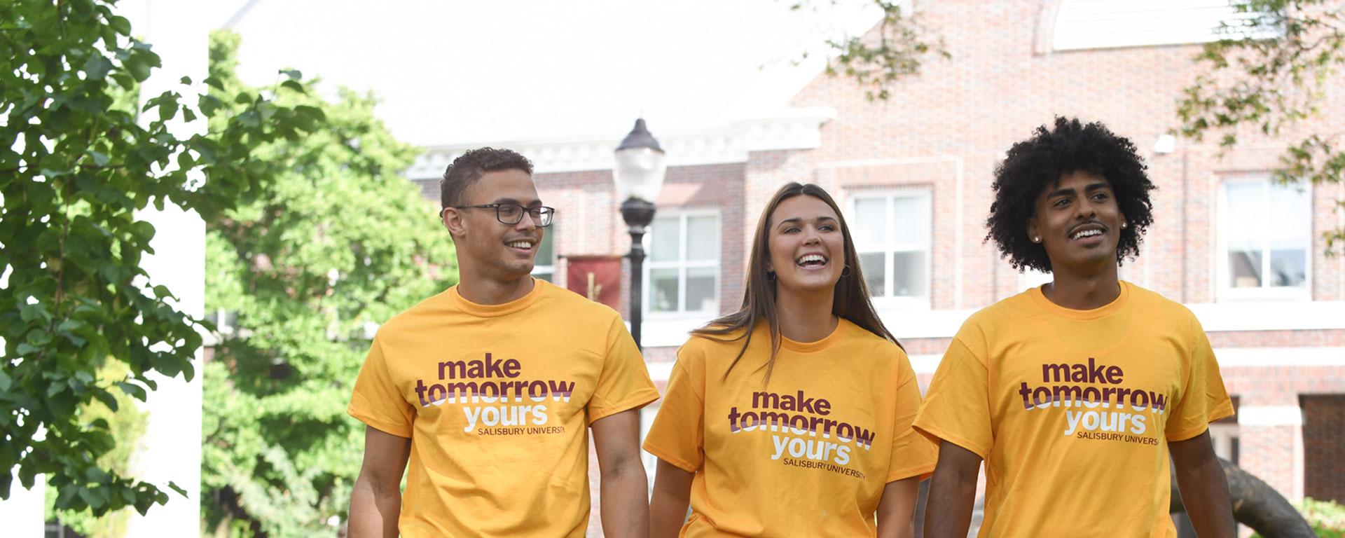 Three students outside wearing make tomorrow yours t-shirts
