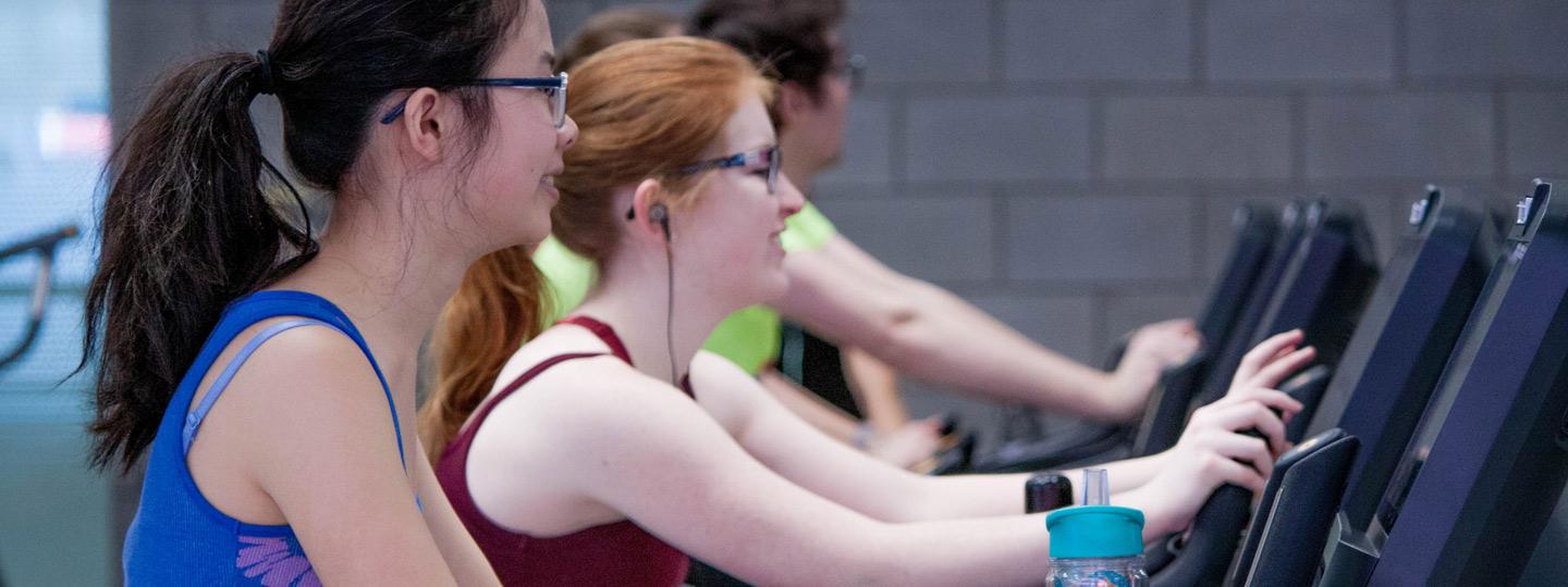 People in university fitness center riding stationary bikes