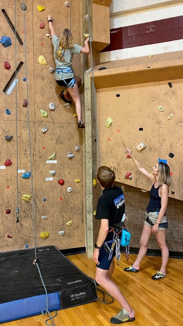 Rock Wall with person Climbing, person belaying and one person watching