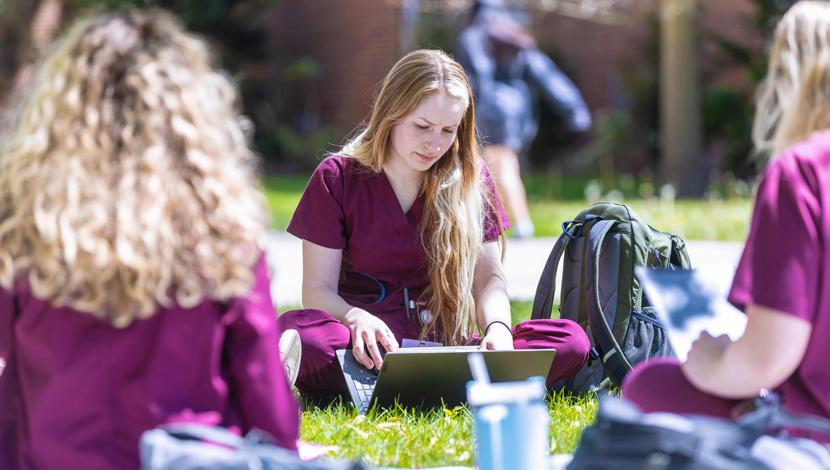 Three nursing students study outside on lawn