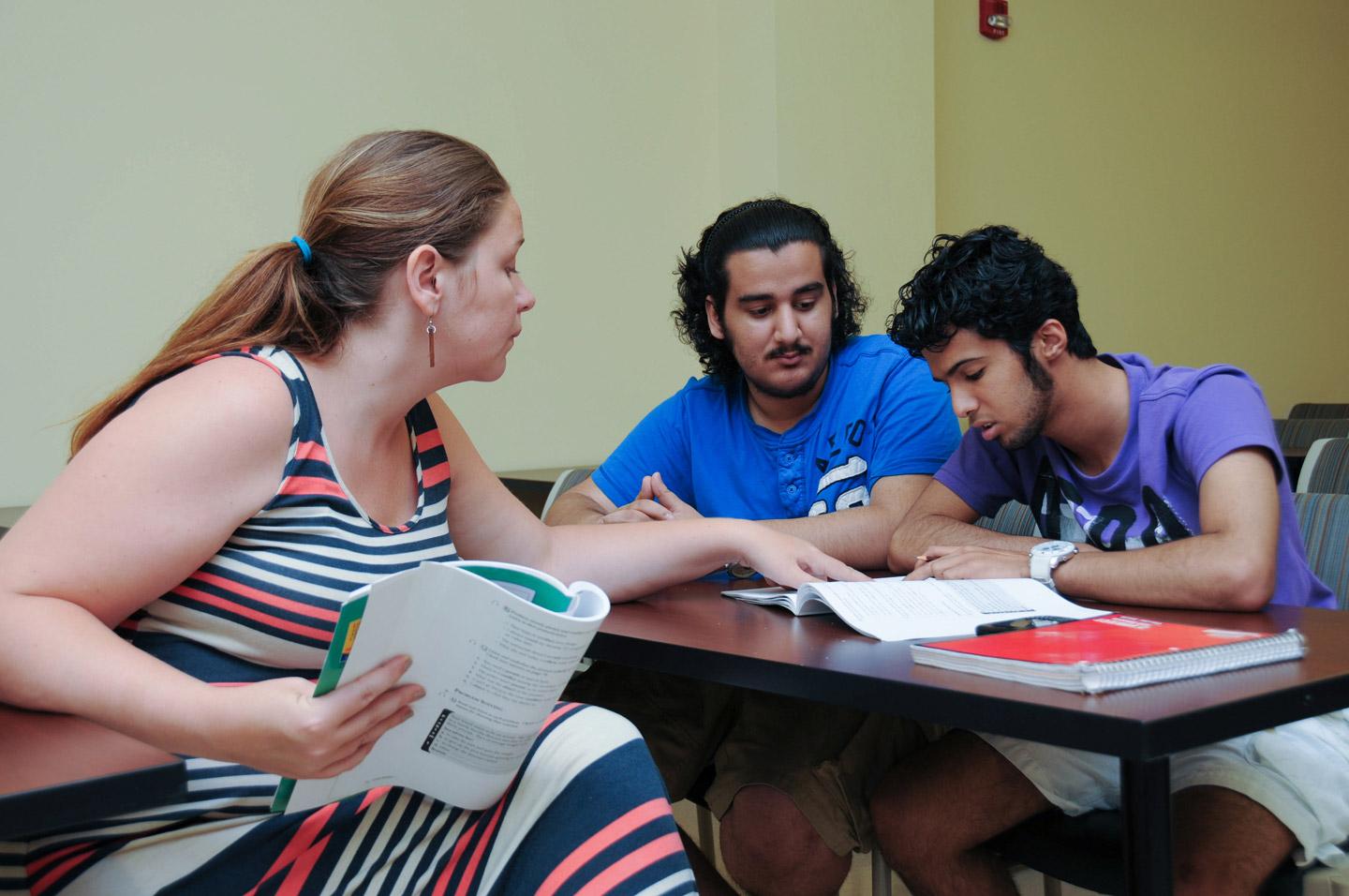 professor sitting with two students, pointing to book