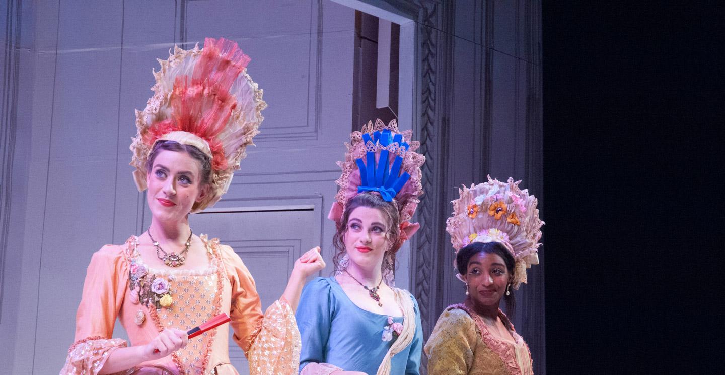 three students dressed in colorful costumes on stage