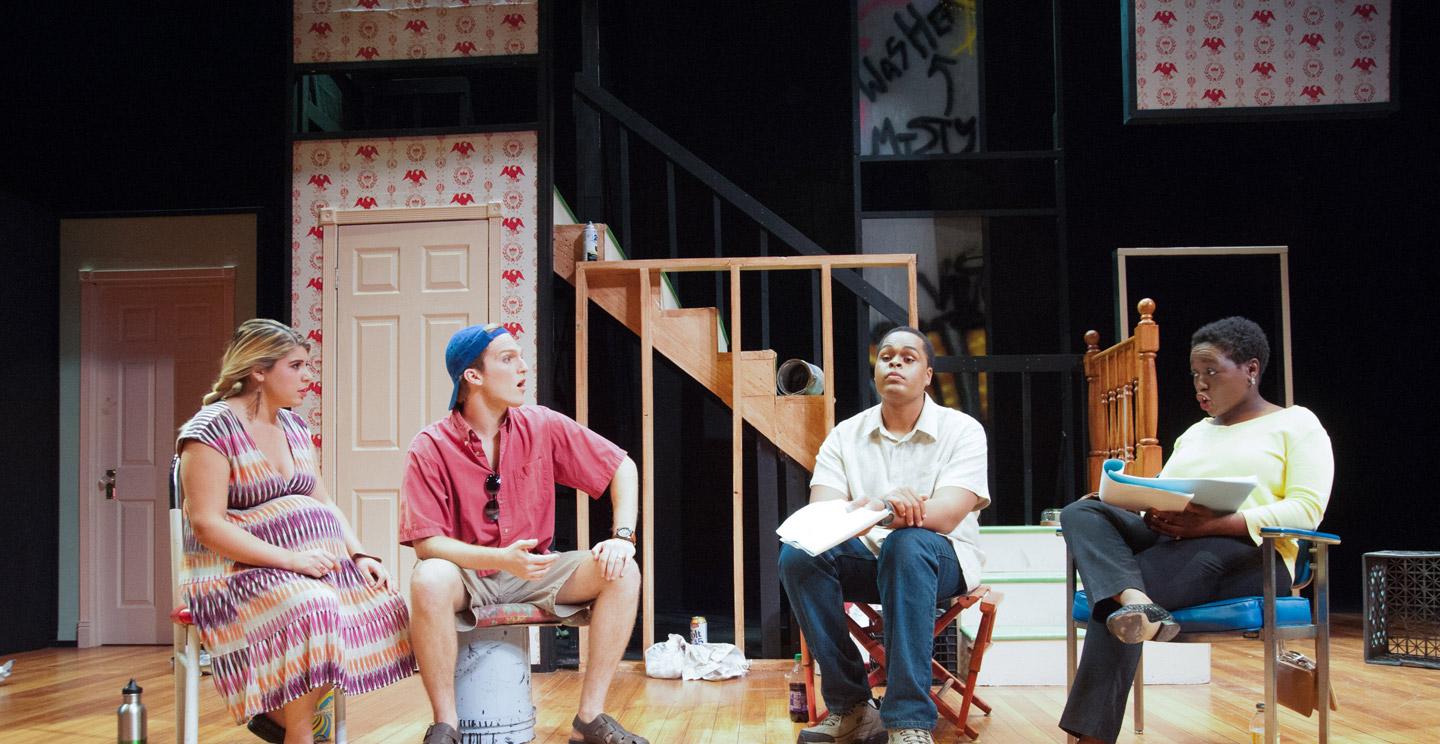 four seated students rehearsing a play on stage