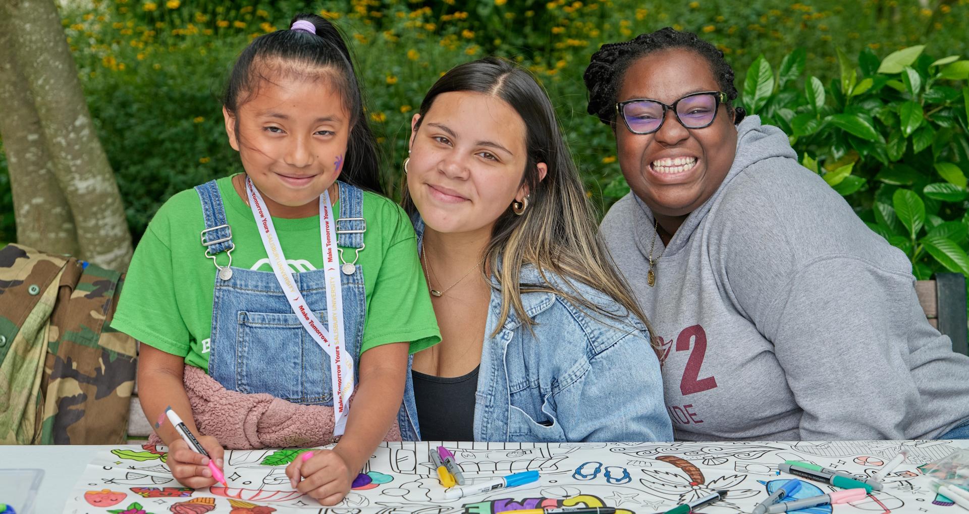 Student works with a mother and child at a table designed to be drawn on