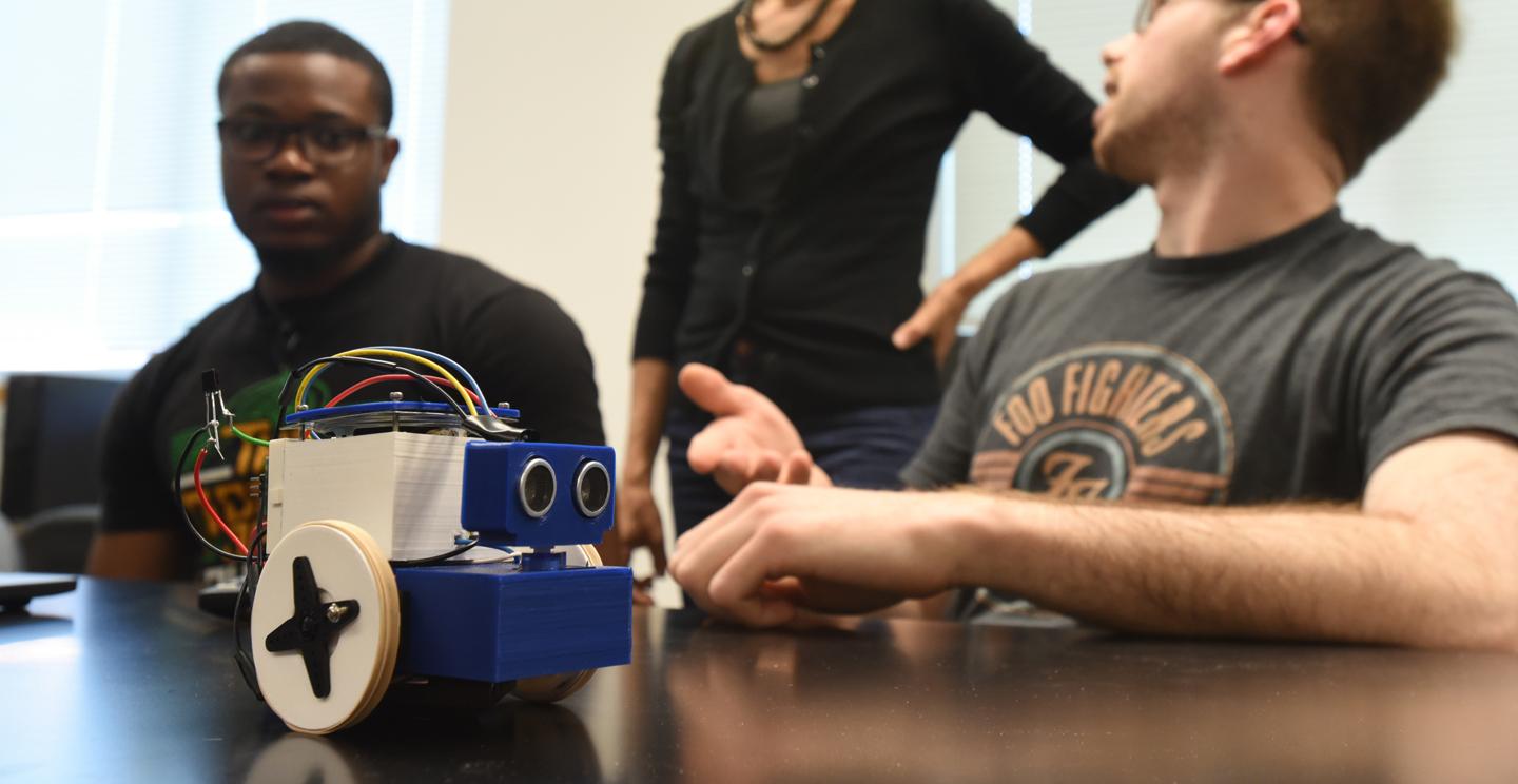 Computer science major gesturing at a robot on a desk