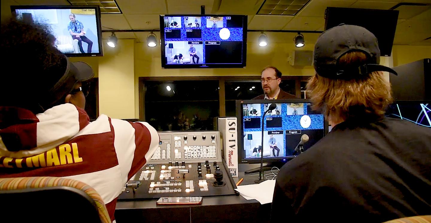 Students studying multimedia journalism work in control room of TV center