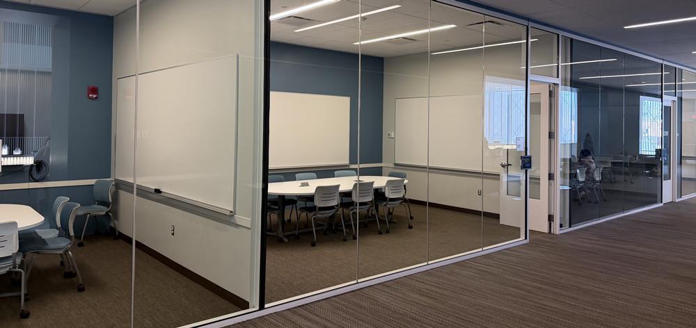 Several study rooms with glass front walls. Each room has a table and several chairs, whiteboards, and a TV.