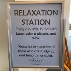 Sign board that reads: Relaxation Station. Enjoy a puzzle, build with Lego, color a picture, and relax. Please be considerate of those who are studying, and keep things quiet.