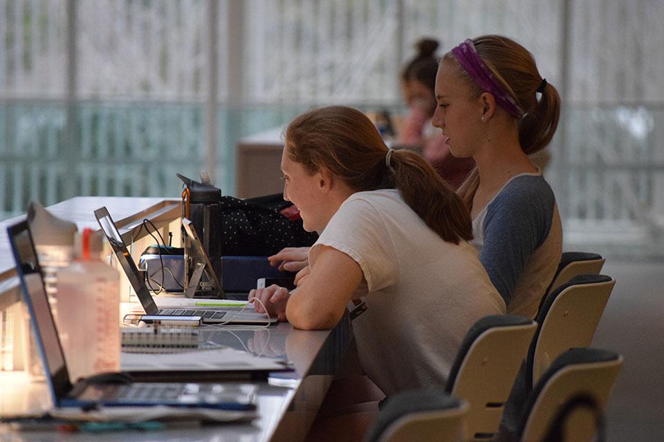 Two students studying on laptops at the atrium bar stools